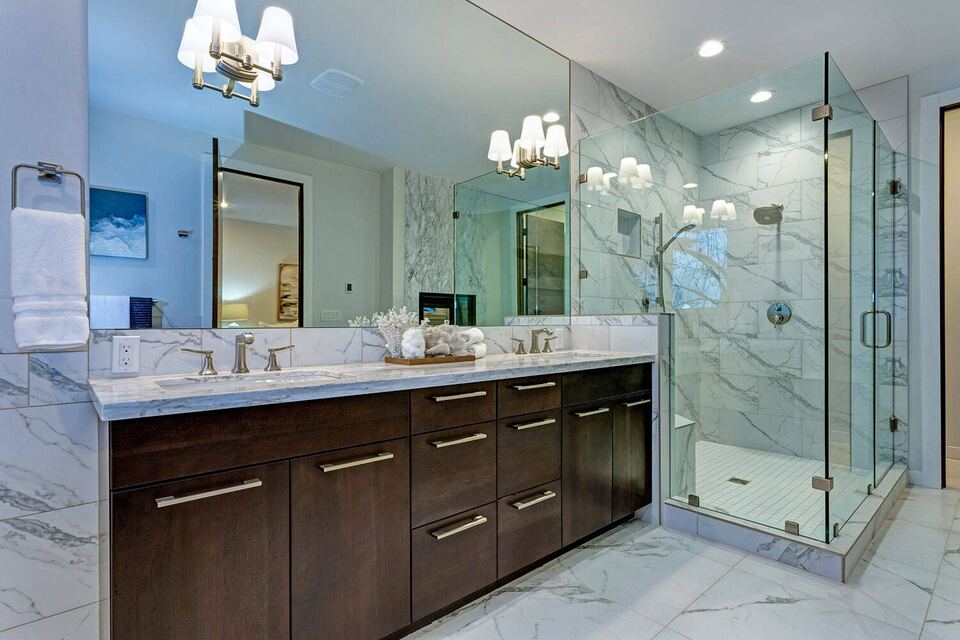 Bright master bathroom with a frameless glass shower enclosure, marble tile and a double vanity