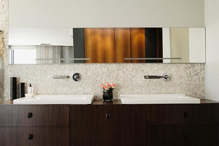 Long frameless vanity mirror over a double sink with dark wood cabinets