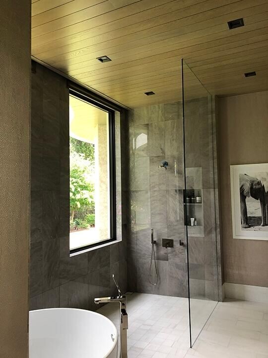 Walk-in shower with a single fixed frameless glass panel and gray stone tile